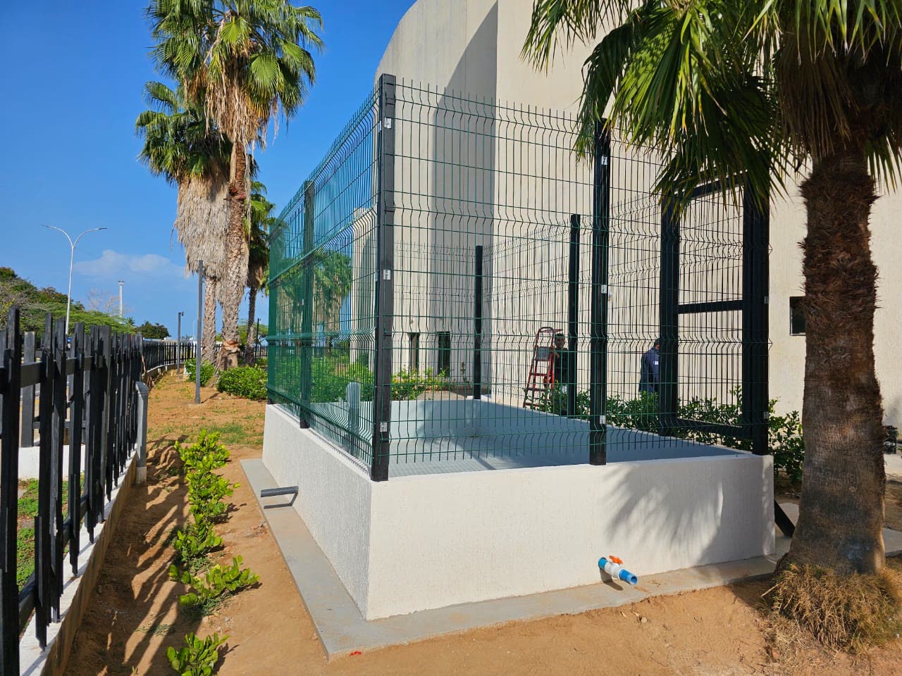 Caseta técnica con cerca de seguridad terminada junto a edificio institucional