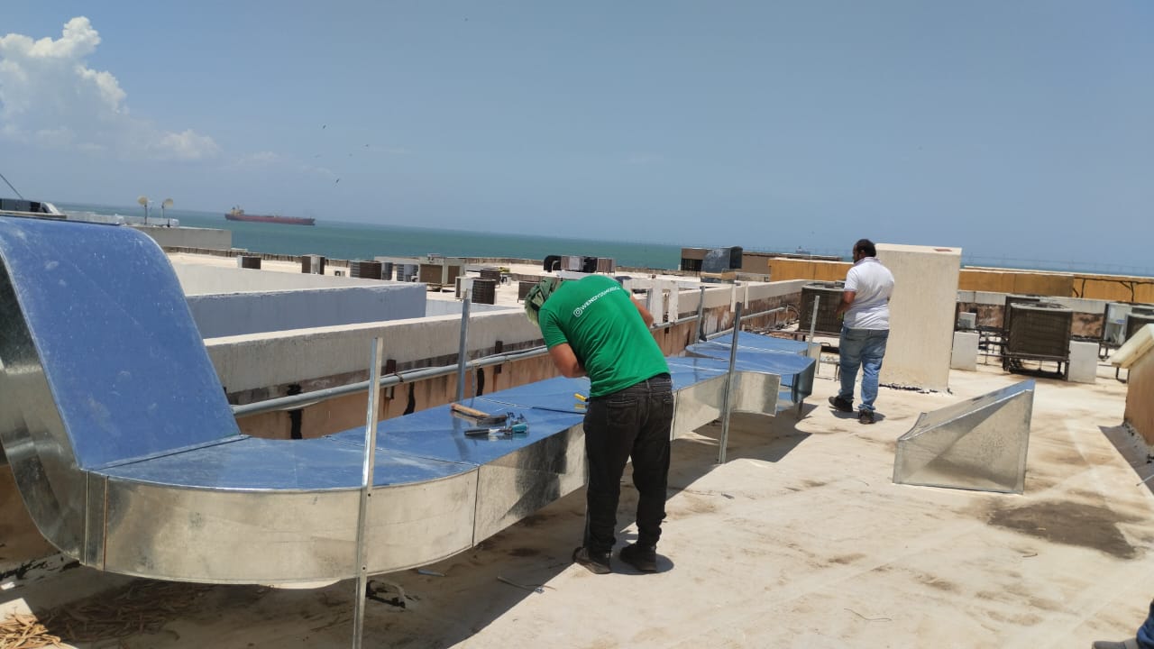 Cuadrilla fabricando ductos galvanizados en azotea frente al lago