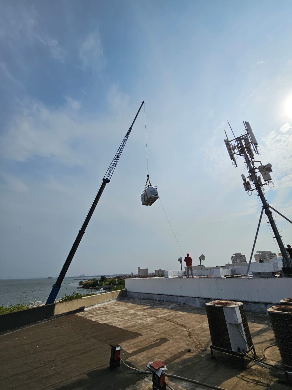 Grúa bajando una unidad de climatización sobre una azotea con el Lago de Maracaibo al fondo