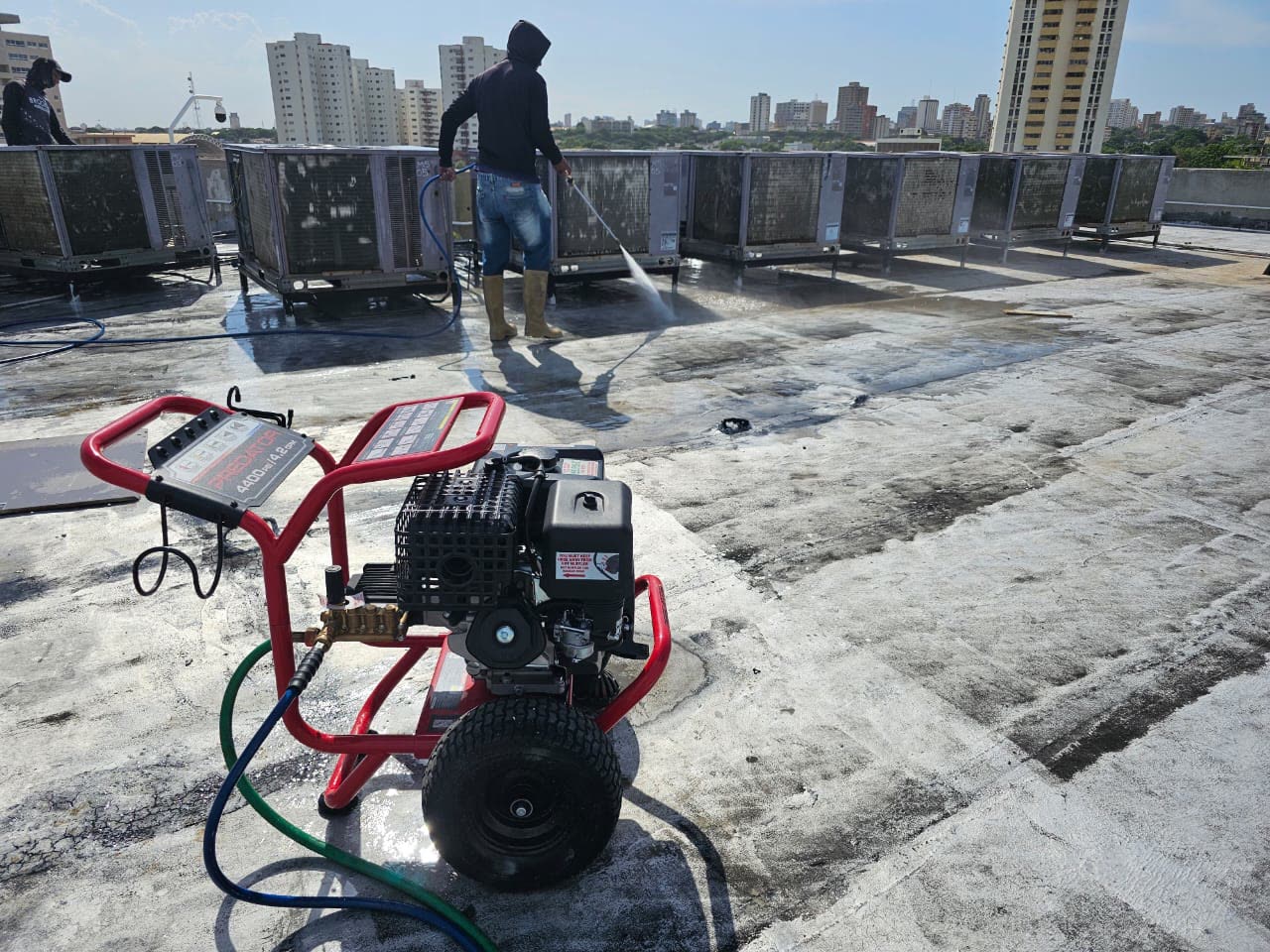 Técnico lavando a presión una fila de unidades de climatización en azotea con la ciudad al fondo